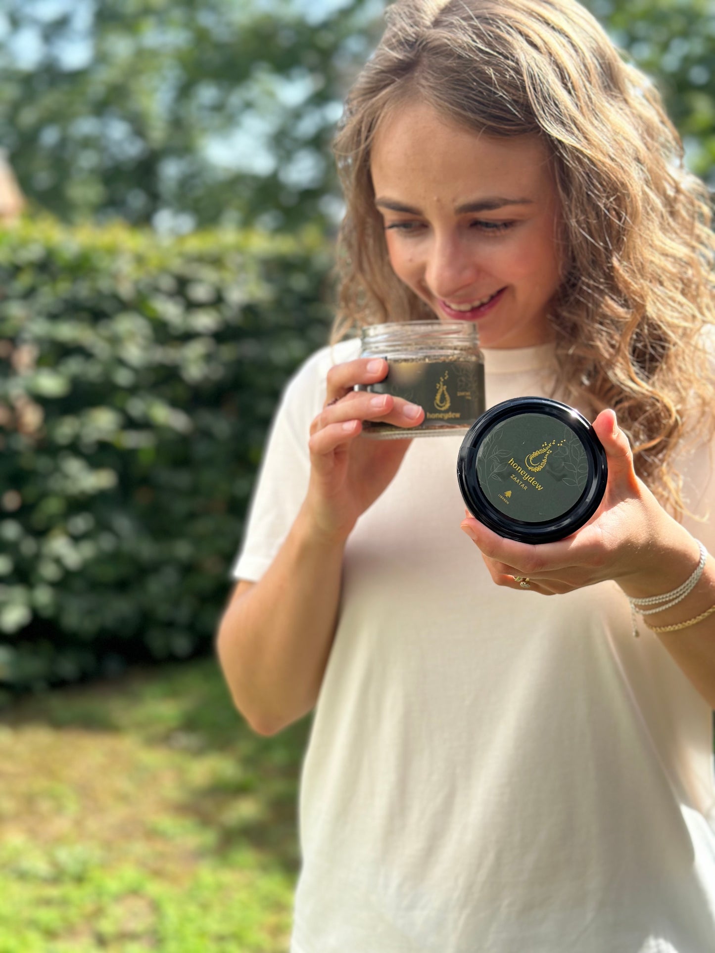Junge Frau mit langem Haar hält ein Glas libanesische Zaatar Mischung und riecht genüsslich daran, schwarzer Deckel mit goldener Beschriftung in der Hand