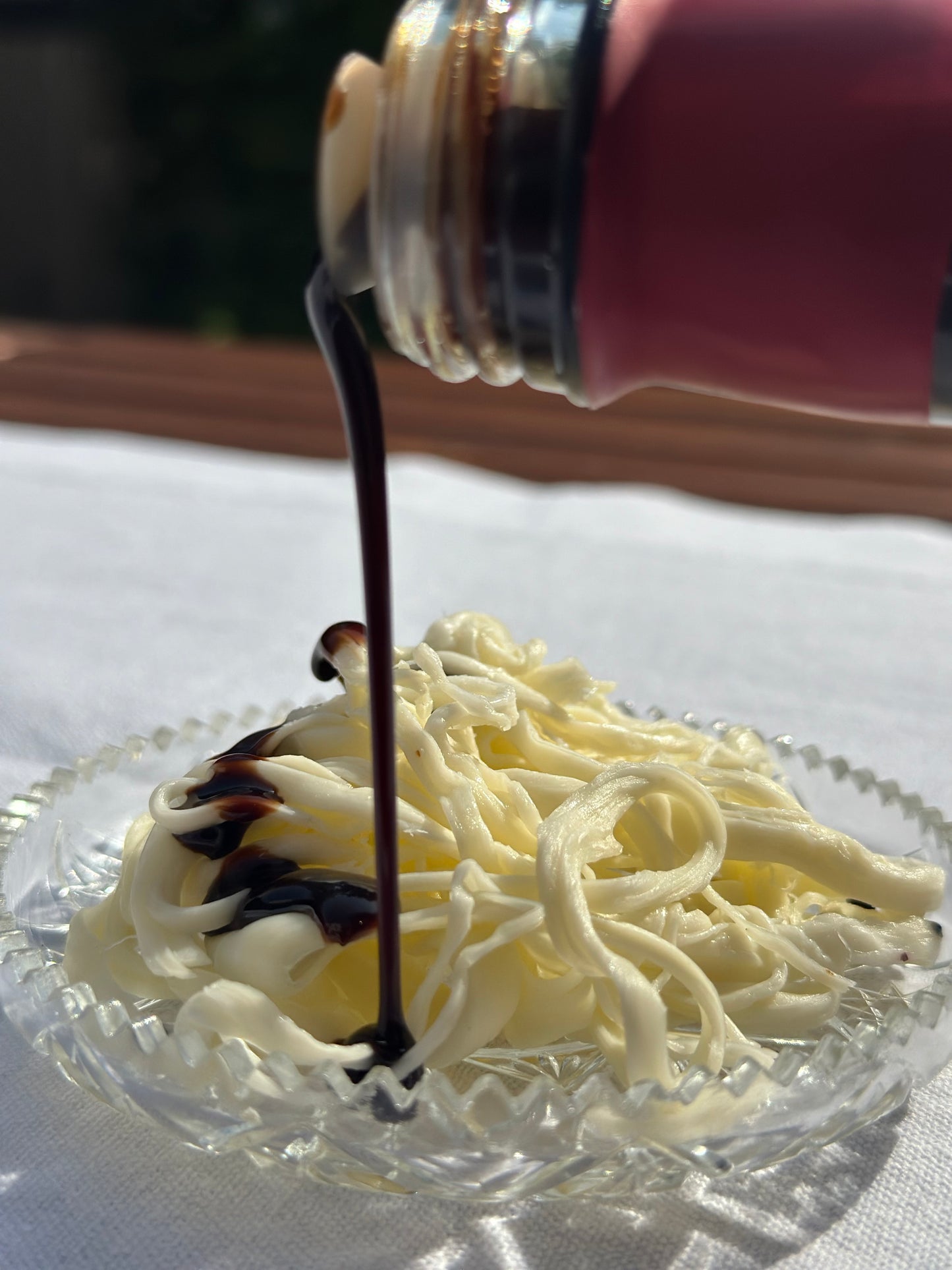 Shanklish-Käse mit honeydew Granatapfelmelasse, glänzendem Strom aus einem Glasbehälter, vor neutralem Hintergrund und Sonnenlicht