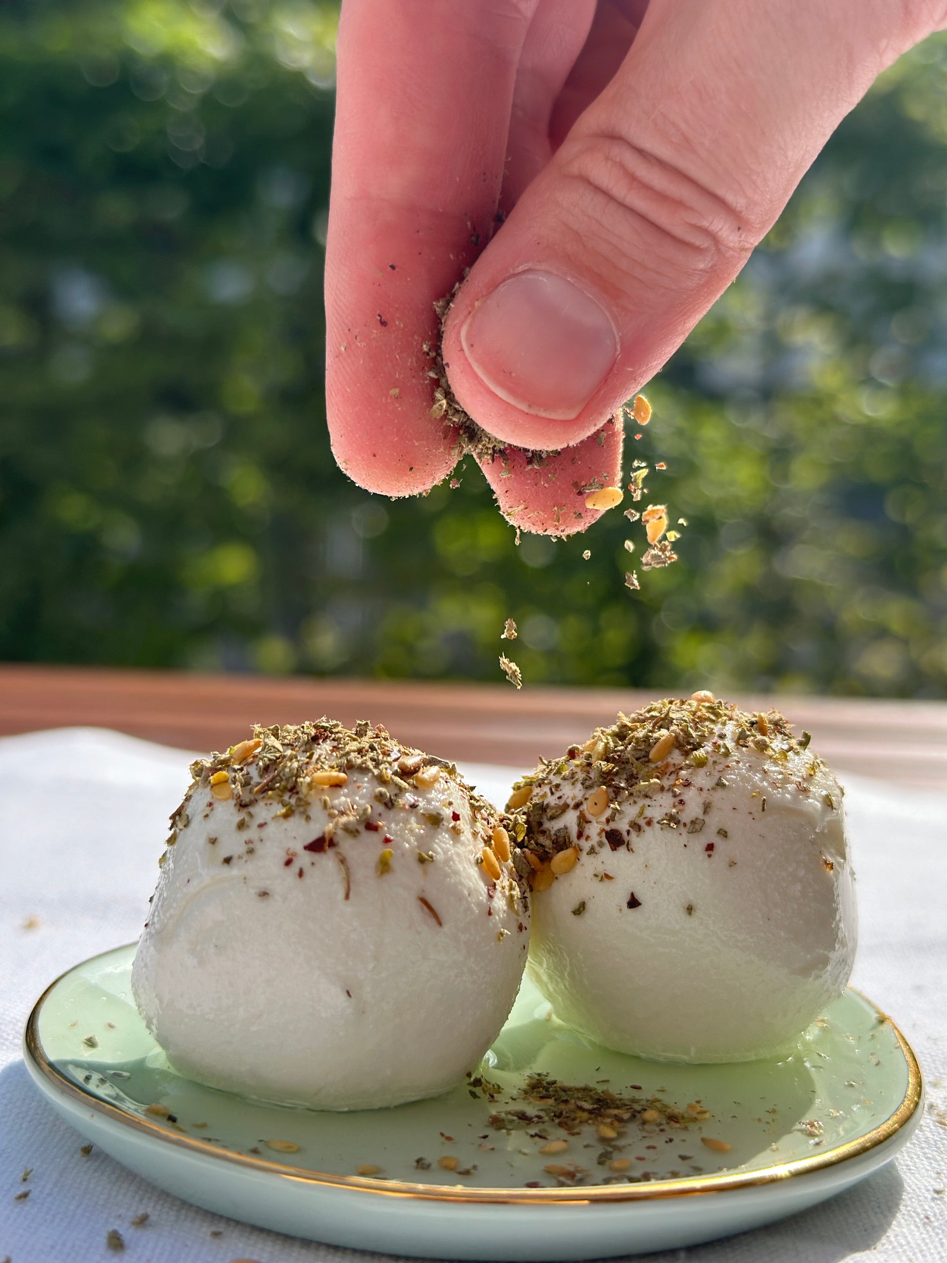 Zwei Labneh-Kugeln auf einem Teller, bestreut mit libanesicher Zaatar Mischung, während Sonnenlicht die Textur und Farben hervorhebt.
