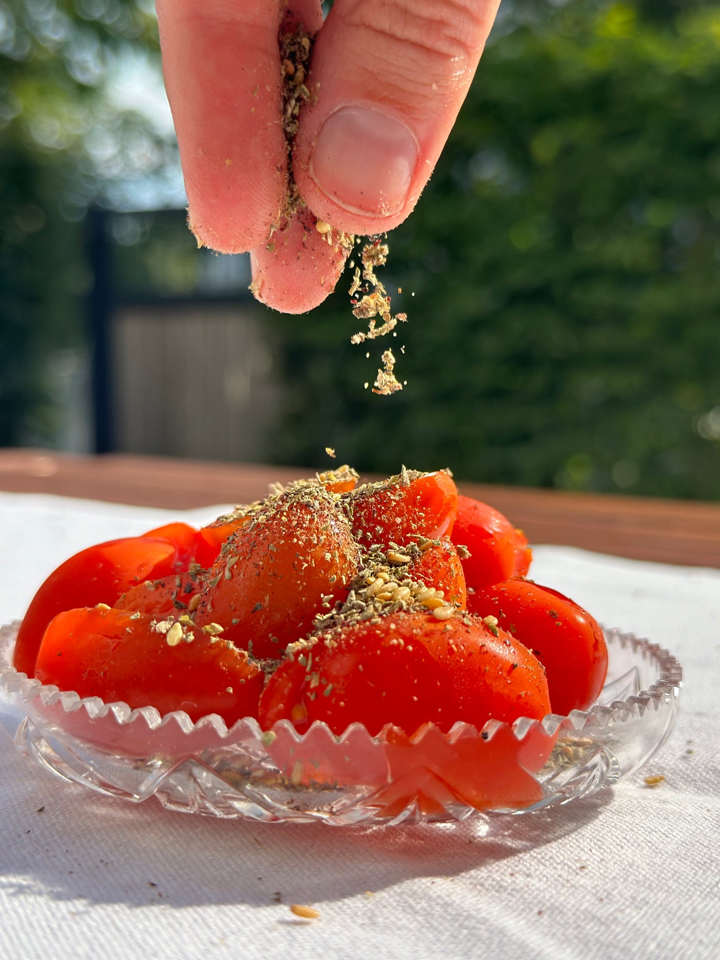 Reife Tomatenstücke in einer Glasschale, bestreut mit libanesischer Zaatar-Mischung, vor natürlichem Licht und grünem Hintergrund