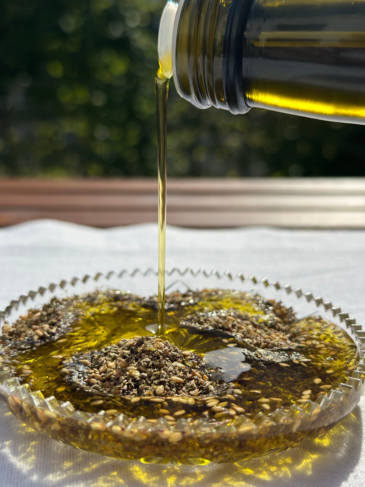 Feiner Strahl goldenen Olivenöls fließt in eine Glasschale mit libanesichen Zaatar Mischung, betont durch Sonnenlicht und glänzende Texturen