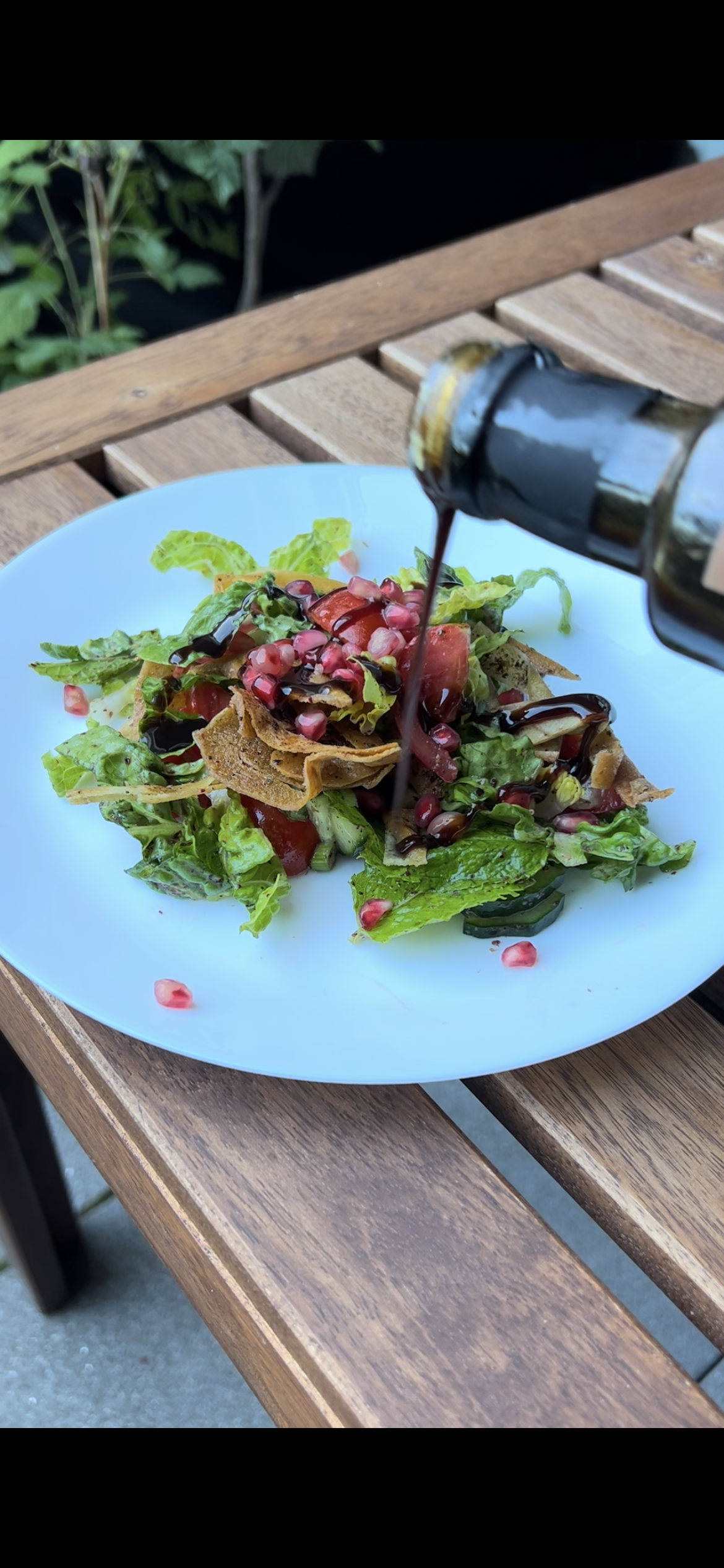 Libanesischer Fattoush-Salat mit knusprigem Brot, Granatapfelkernen und frischem Gemüse, beträufelt mit Granatapfelmelasse, serviert auf einem weißen Teller