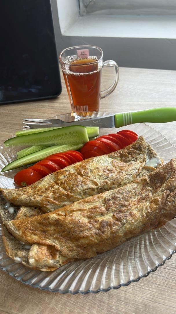 Libanesisches Frühstück mit einem Za'atar-Omelette, geschnittenen Gurken und Tomaten, serviert auf einem Glasteller, begleitet von einem Glas schwarzem Tee